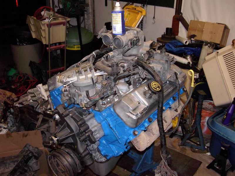 V8 engine on stand with blue block and aluminum intake in cluttered garage