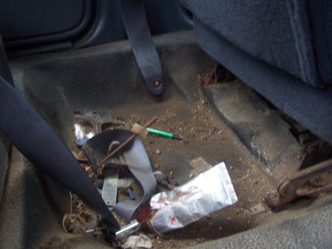 2001 Ford Crown Victoria - The interior floor of a car is covered in dirt and debris, with a seatbelt and a tube of ointment visible.