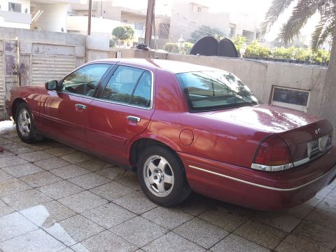 1998 Ford Crown Victoria - This red 1998 Ford Crown Victoria is parked outside a building.