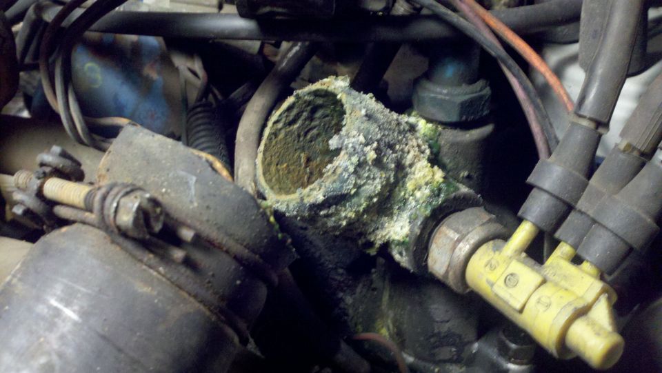 Corroded engine part with green and yellow buildup, surrounded by wires and hoses