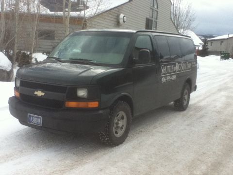 2006 Ford E350 - A black Chevrolet Express van, marked as a shuttle for Big Sky Taxi, sits parked on a snow-covered road.