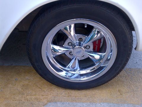 1965 Ford Mustang - Close-up of a chrome wheel and red brake caliper, with Supermotors.net watermark.