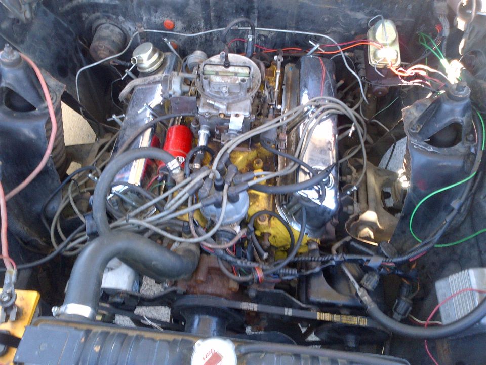 Engine bay showing a V8 engine with chrome valve covers, carburetor, and distributor