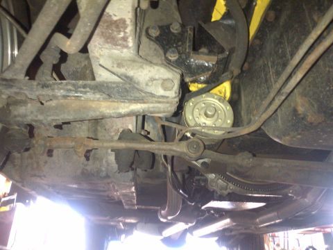 1965 Ford Mustang - The underside of a vehicle reveals rusted suspension parts and exhaust systems.