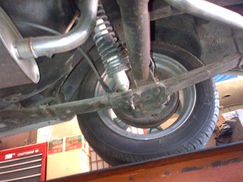1965 Ford Mustang - The rear suspension and exhaust system of a vehicle are visible from below, with a tire and wheel in the background.