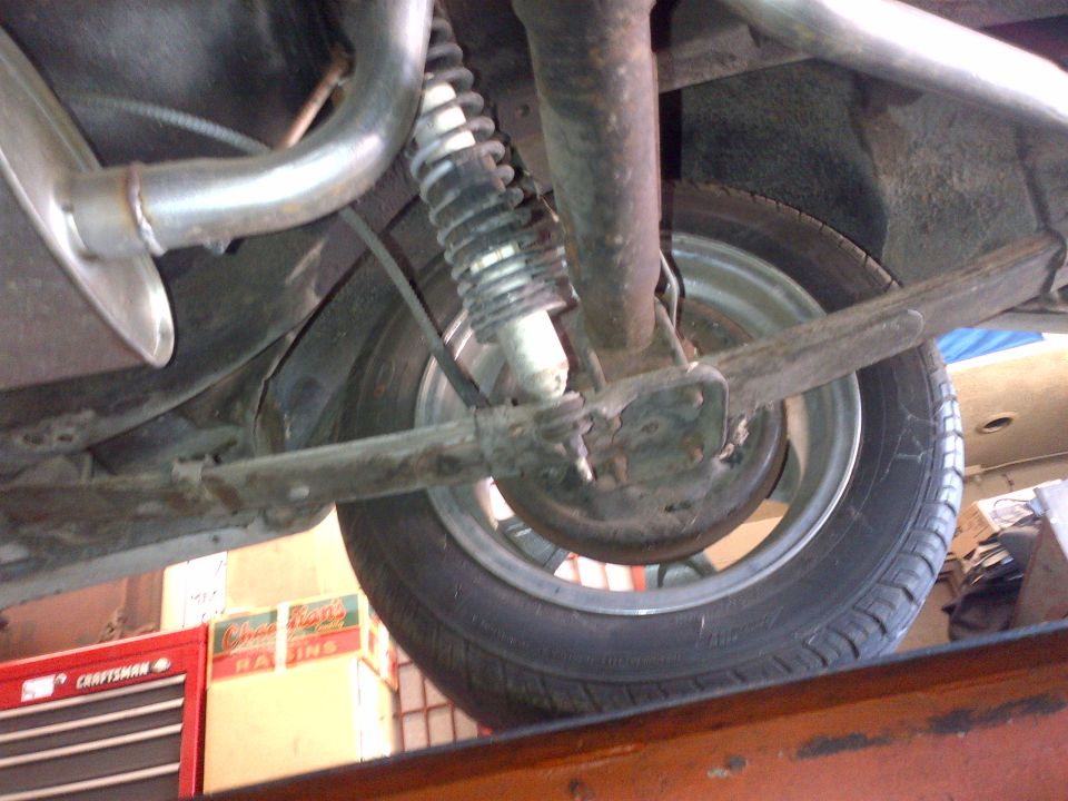 Underside view of a car's rear suspension, showing the axle, leaf spring, shock absorber, and exhaust pipe