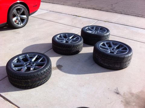 2010 Dodge Challenger - A red Dodge Challenger is partially visible next to four new tires and wheels laid out on a concrete surface.