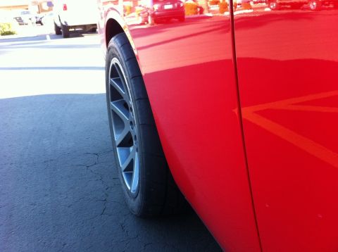 2010 Dodge Challenger - Close-up of a red car's rear quarter panel and wheel, aftermarket rims and Nitto tires. The vehicle appears to be a 2010 Dodge Challenger.