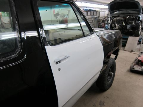 1987 Dodge 1500 - A truck door in a workshop, with another vehicle undergoing repairs in the background.