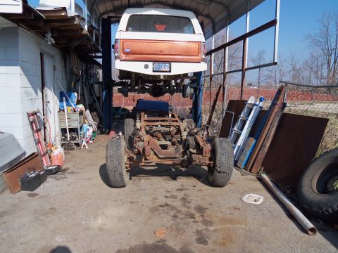 1987 Ford Ranger - A truck is elevated on a lift, with its chassis exposed below. The cab is white with an orange accent panel.