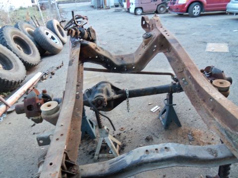1987 Ford Ranger - A disassembled vehicle frame and axle sit on jack stands, with spare tires piled to the side.