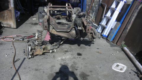 1987 Ford Ranger - A disassembled truck chassis sits in a yard, with the front suspension components detached from the frame.