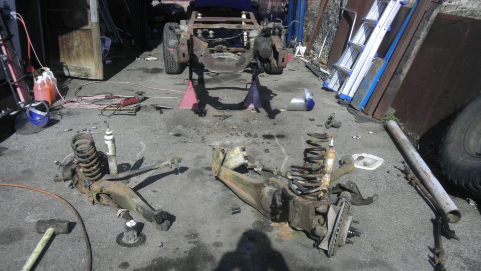 Disassembled vehicle chassis on jack stands with suspension components scattered on the ground