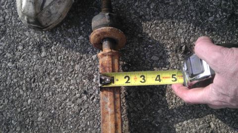 1987 Ford Ranger - A rusty metal part is measured with a tape measure on an asphalt surface.