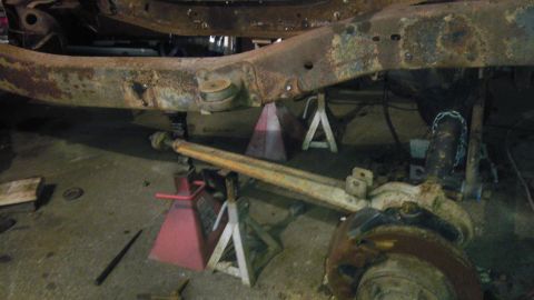 1987 Ford Ranger - The heavily rusted undercarriage of a vehicle is supported by jack stands, indicating it is undergoing repairs or restoration.