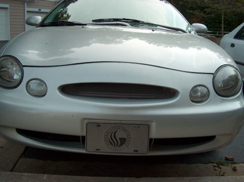 1998 Ford Taurus - A silver sedan is parked in front of a building, with another vehicle visible to the right.