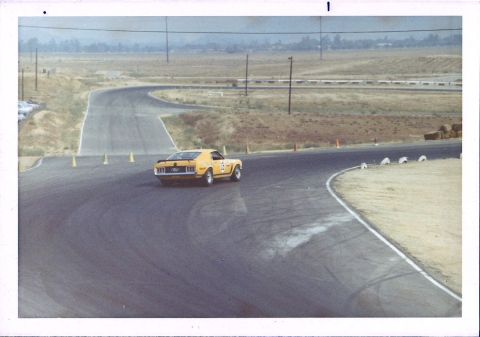 1973 Ford Mustang - A yellow 1970s muscle car races around a track, kicking up dust on the turn.