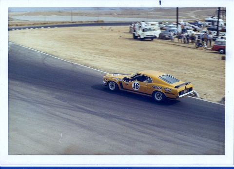 1973 Ford Mustang - A yellow 1970 Ford Mustang Boss 302 race car navigates a turn on a sunny day at the track.