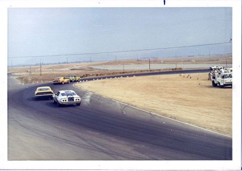 1973 Ford Mustang - Several cars race on a track with dry, dusty surroundings under a hazy sky.