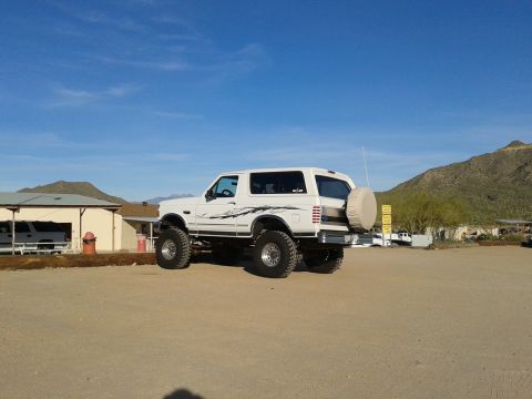 1996 Ford Bronco - This lifted 1996 Ford Bronco features custom side graphics and a rear-mounted spare tire, seen in a desert landscape.