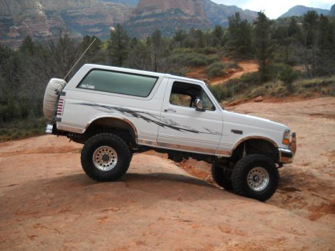 1996 Ford Bronco - A white 1996 Ford Bronco navigates a rocky trail, its off-road capabilities.
