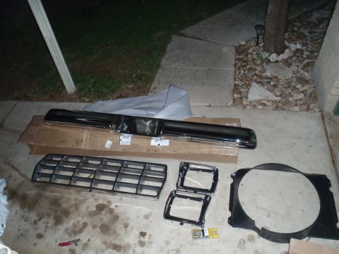 1979 Ford Bronco - Car parts including a grille, bumper, and fan shroud are displayed on a concrete surface.
