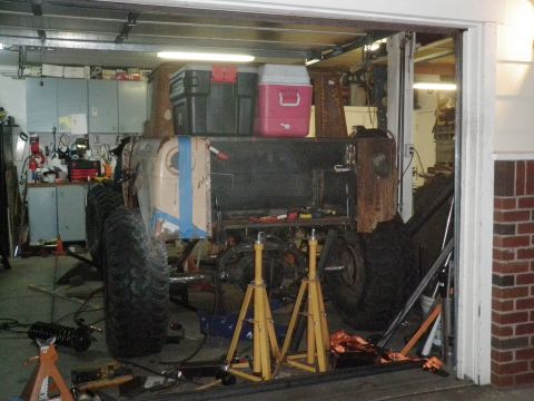 1961 International Scout 800 - A heavily modified vehicle is undergoing work in a garage, supported by yellow jack stands.