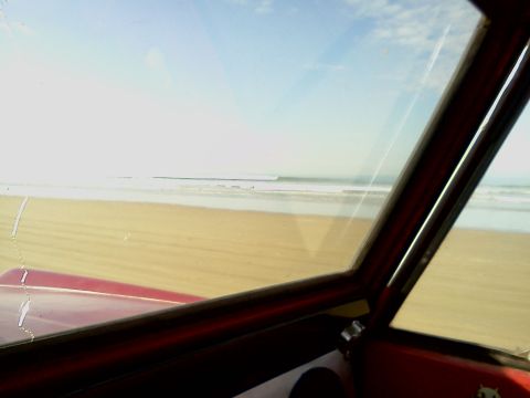 1968 Ford Bronco - The view from the driver's seat shows a sandy beach and ocean waves under a bright sky.