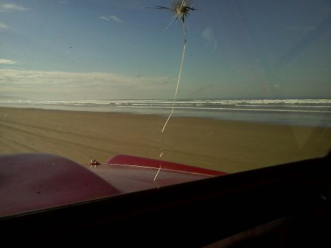 1968 Ford Bronco - View from inside a red vehicle driving on a sandy beach with ocean waves in the background.