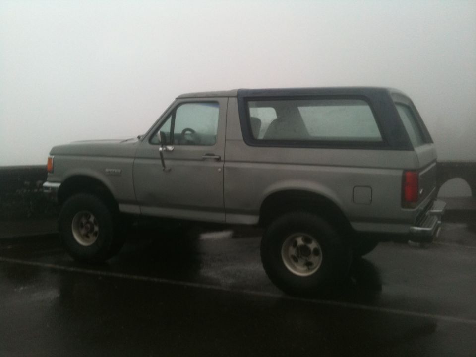 Side view of a gray SUV with a dark top and off-road tires parked on a wet surface