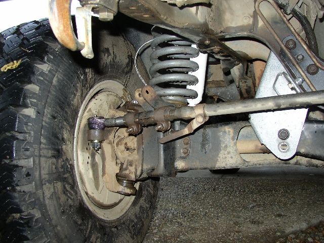 Close-up of a leaf-sprung front suspension, drum brake backing plate and steering linkage underneath a truck
