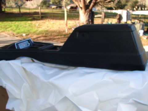 1973 Ford Ranchero - A black automotive center console is shown, partially covered by white sheeting, with a blurred outdoor background.