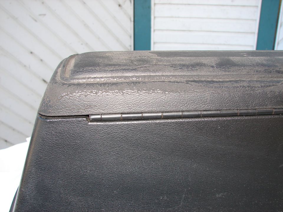 Close-up of a black plastic lid with a visible hinge. The lid has a textured surface