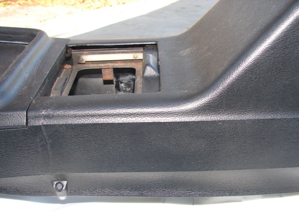 Close-up of a black plastic car interior part with an open compartment showing metal and rust