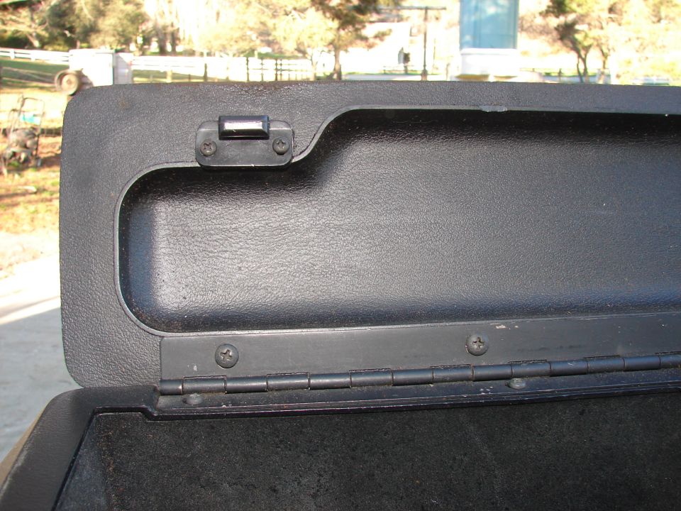 Close-up of an open black plastic storage compartment lid with hinges and a small latch