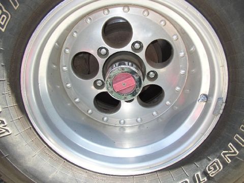 1989 Ford Bronco - This image shows a close-up of a vehicle's wheel, a red and chrome hubcap and tire sidewall details.
