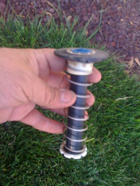 1968 Ford Mustang - A person holds a part of a sprinkler head, showing the spring mechanism against a grassy background.