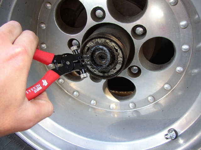 Hand using red snap-ring pliers on a greasy wheel hub spindle nut inside an aluminum wheel