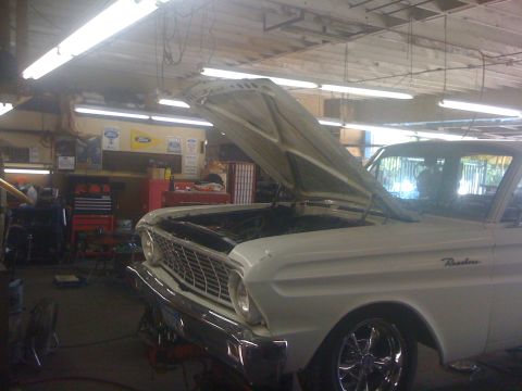 1964 Ford Ranchero - A white 1964 Ford Ranchero is parked in a garage with its hood up, revealing the engine bay.