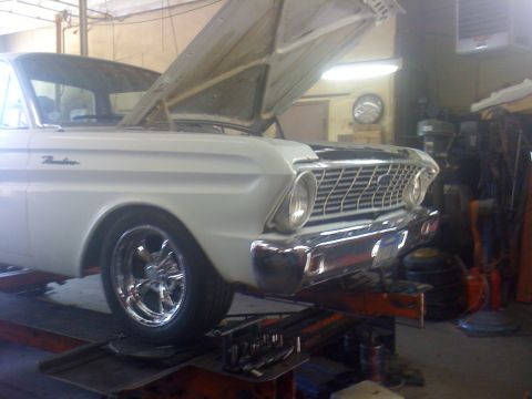 1964 Ford Ranchero - A white 1964 Ford Ranchero is shown on a lift in a garage, with its hood open, revealing custom chrome wheels.