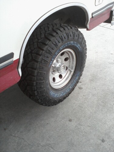 1989 Ford Bronco - Close-up of a 1989 Ford Bronco's rear wheel and fender, showing off-road tires and a two-tone paint scheme.
