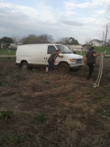 1989 Ford Bronco - A white van is stuck in a muddy field, with two individuals attempting to free it.