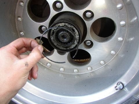1989 Ford Bronco - A hand is shown removing a spring clip from a wheel hub assembly, likely during maintenance or repair.