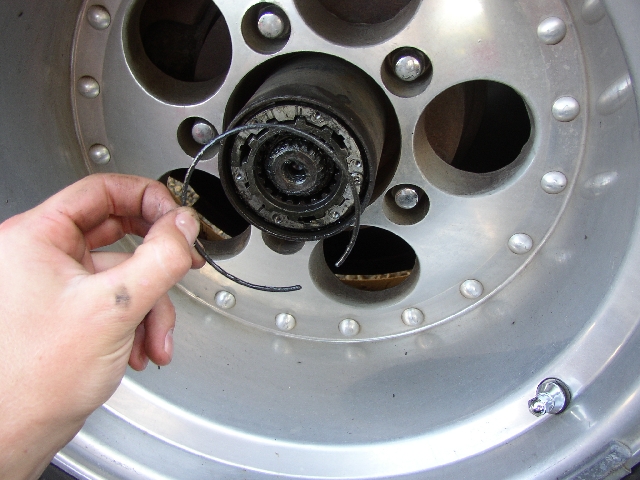 Hand holding snap ring at greasy locking hub inside silver alloy wheel
