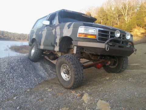 1995 Ford Bronco - Modified 1995 Ford Bronco in camouflage paint is shown off-roading on a gravel incline.