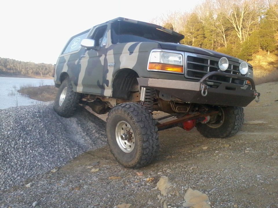 1995 Ford Bronco with camouflage paint climbing a gravel pile near a body of water
