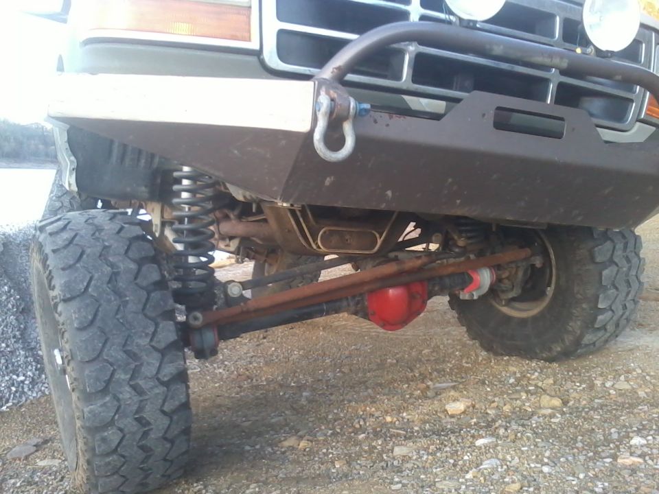Front view of a modified 1992 Ford Bronco's suspension, showing large tires, heavy-duty bumper, and red differential