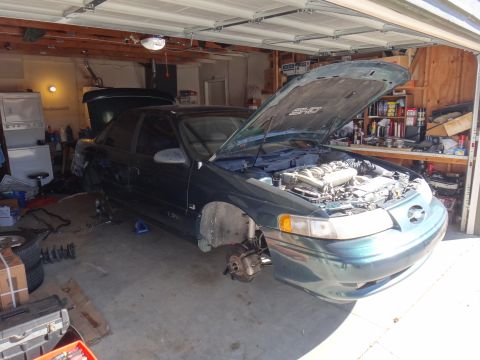 1993 Ford Taurus - A green 1992 Ford Taurus is undergoing maintenance in a garage, with its hood up and front wheels off.