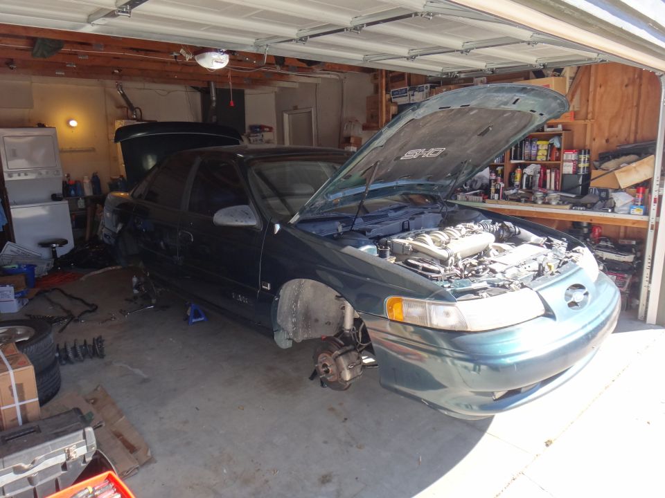 Green 1992 Ford Taurus with hood open, front wheels removed, in a garage