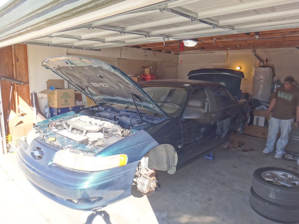 Dark green 1993 Ford Taurus coupe with hood open, front wheels removed